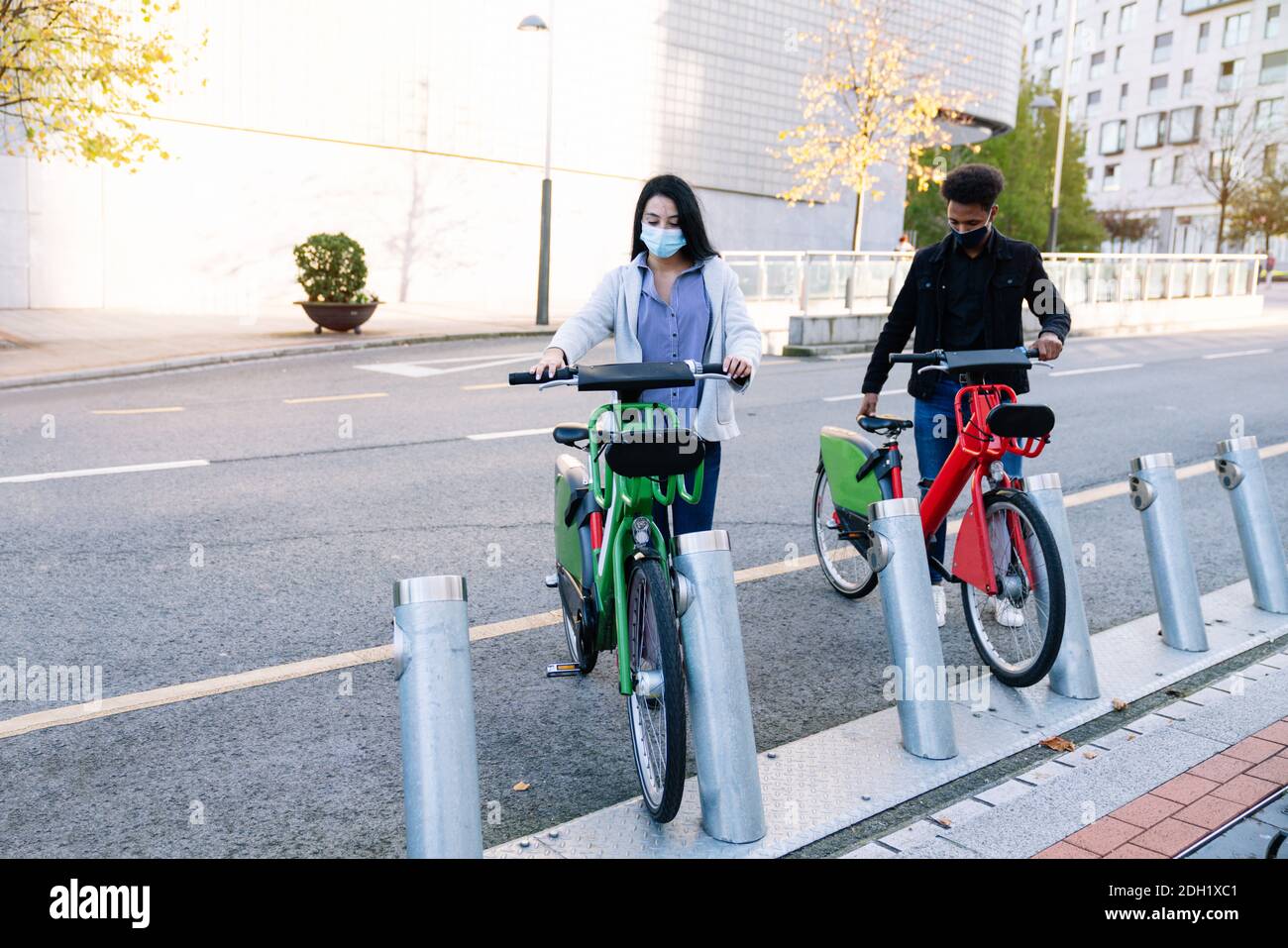 Ein junger Marokkaner und ein kaukasisches Mädchen pflücken Bis ein gemieteten Elektro-Fahrrad in der Straße Fahrrad-Parkplatz Und tragen eine Gesichtsmaske für die 2 Stockfoto