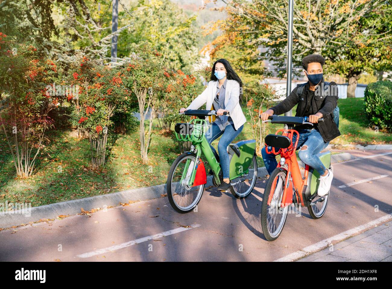Vor zwei jungen Mann und Frau reiten entlang ein Fahrradweg mit einem gemeinsamen Elektro-Fahrrad in einem schönen park mit vielen Bäumen bei Sonnenuntergang tragen ein f Stockfoto