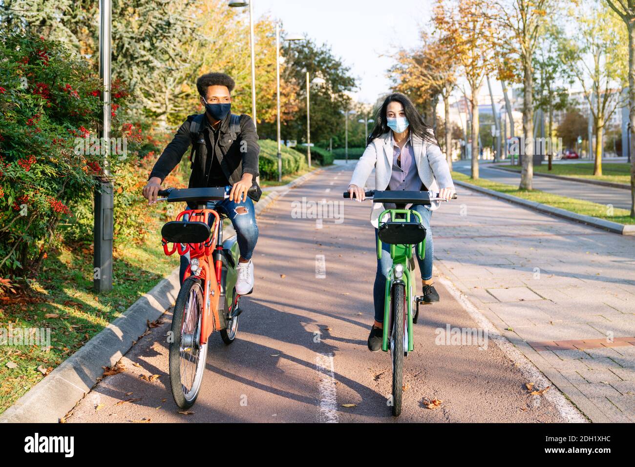 Vor zwei jungen Mann und Frau reiten entlang ein Fahrradweg mit einem gemeinsamen Elektro-Fahrrad in einem schönen park mit vielen Bäumen bei Sonnenuntergang tragen ein f Stockfoto