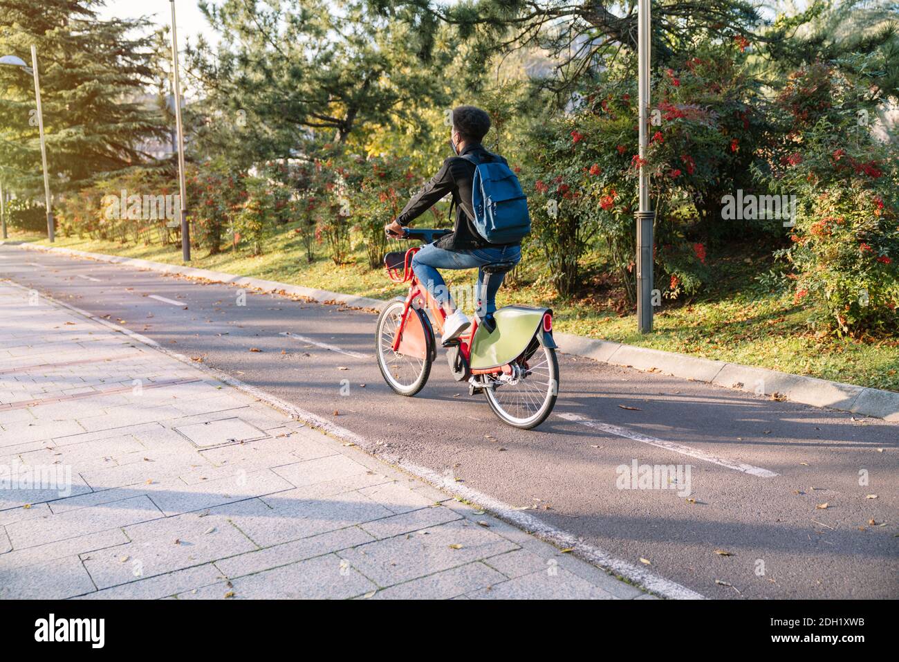 Junger Mann ein marokkanischer Student auf einem gemeinsamen E-Bike in einem schönen Park mit vielen Bäumen bei Sonnenuntergang, trägt eine Gesichtsmaske für die Coronavirus pand Stockfoto