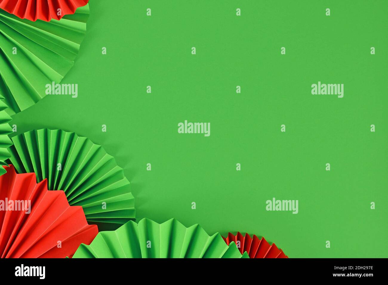 Rote und grüne Papierrosetten in traditionellen Weihnachtsfarben Auf der Seite des grünen Hintergrunds mit leerem Kopierbereich Stockfoto