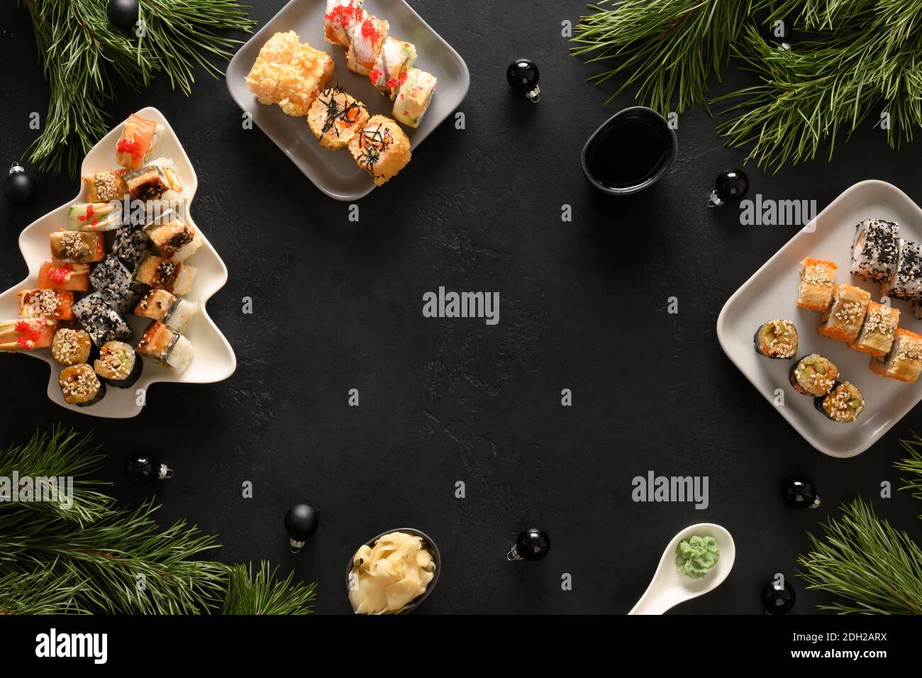 Weihnachtliche Speisen, Sushi-Set und Weihnachtsdekoration auf schwarzem Hintergrund. Speicherplatz kopieren. Blick von oben. Flache Lay-Optik. Silvesterparty. Stockfoto