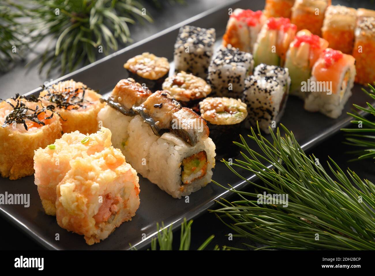Weihnachtsessen mit Sushi-Set mit Weihnachtsdeko auf schwarzem Hintergrund. Nahaufnahme. Weihnachtsfeier oder Neujahrsparty. Stockfoto