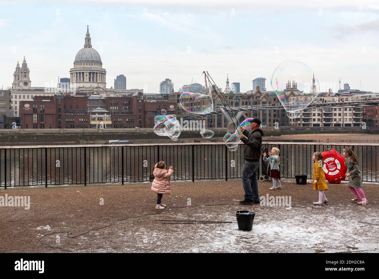 Ein Mann, der Kinder mit einem Bubble Zauberstab in der Nähe der Millennium Bridge mit der St. Paul's Cathedral im Hintergrund unterhält, London Stockfoto
