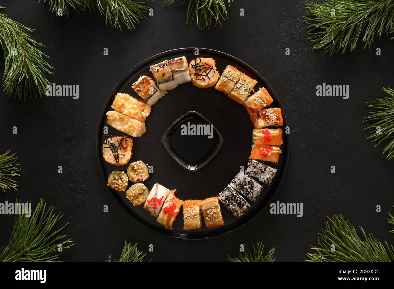 Sushi-Set als Weihnachtskranz verzierte Tannenzweige auf schwarzem Hintergrund. Blick von oben. Speicherplatz kopieren. Lieferung von Lebensmitteln. Stockfoto