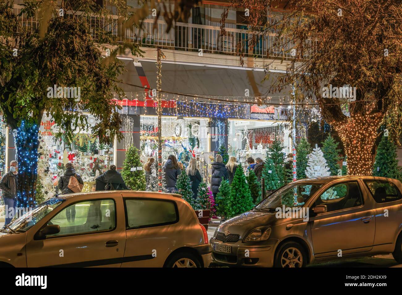 Thessaloniki, Griechenland - 8. Dezember 2020: Hellenic Weihnachtsgeschäft mit Kunden warten auf den Eingang.Menge in der Schlange außerhalb beleuchtet Nacht Blick auf dekorierten saisonalen Speicher. Stockfoto