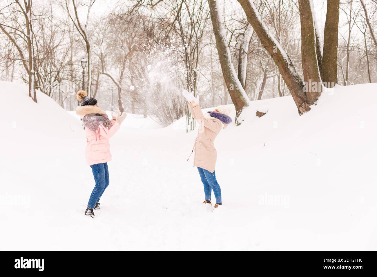 Zwei Mädchen spielen Schneebälle im Winter im Wald. Schwestern in einem warmen Kleid haben Spaß mit Schnee im Winter Stockfoto