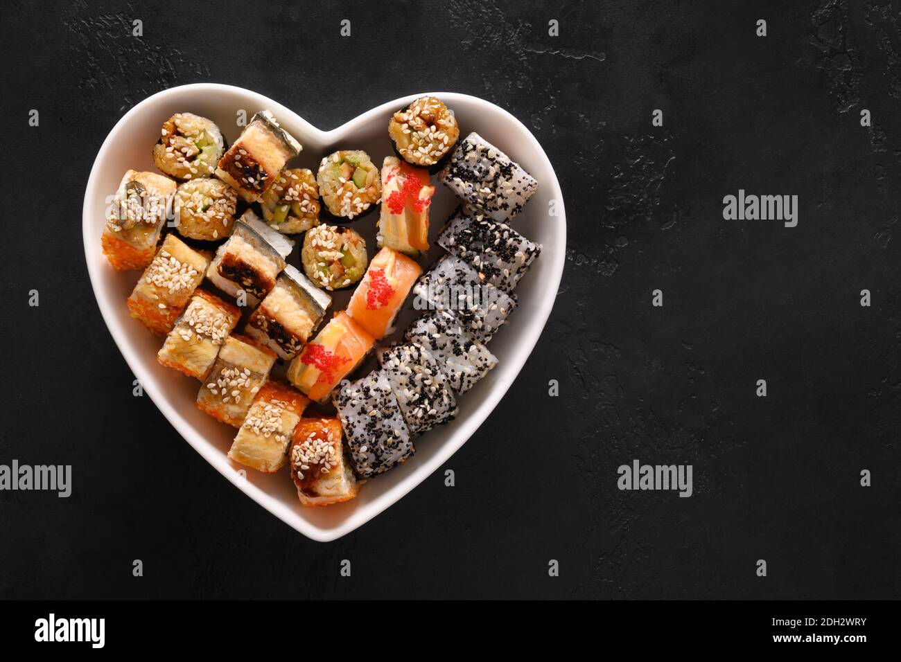 Sushi in Teller als Herz auf schwarzem Hintergrund. Valentinstag Essen Liebe Konzept. Blick von oben. Leerzeichen für Text. Flache Lay-Optik. Stockfoto