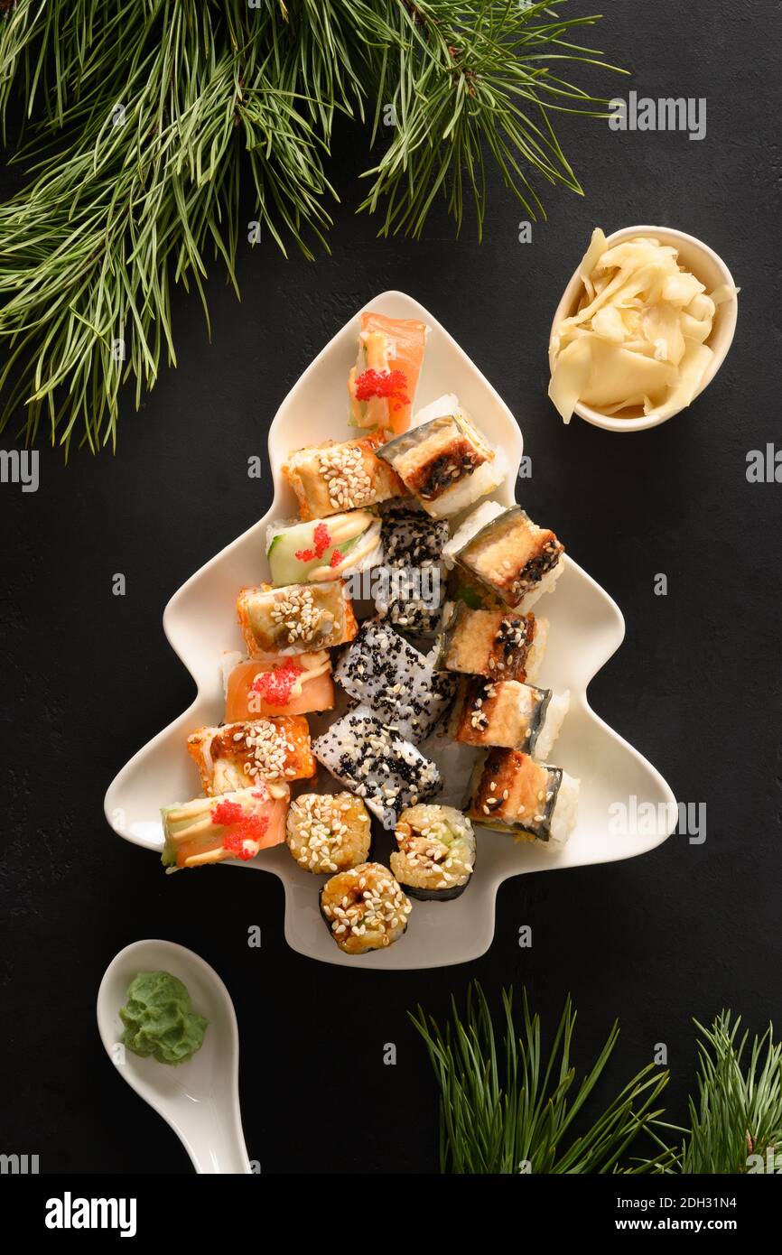 Sushi-Set serviert in Teller als Weihnachtsbaum mit festlicher Dekoration auf schwarzem Hintergrund. Blick von oben. Stockfoto