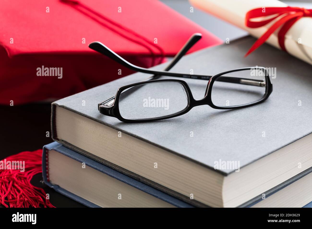 Abschlusskappe und -Brille auf gestapelten Büchern, die akademische Leistungen und Lernerfolge hervorheben Stockfoto