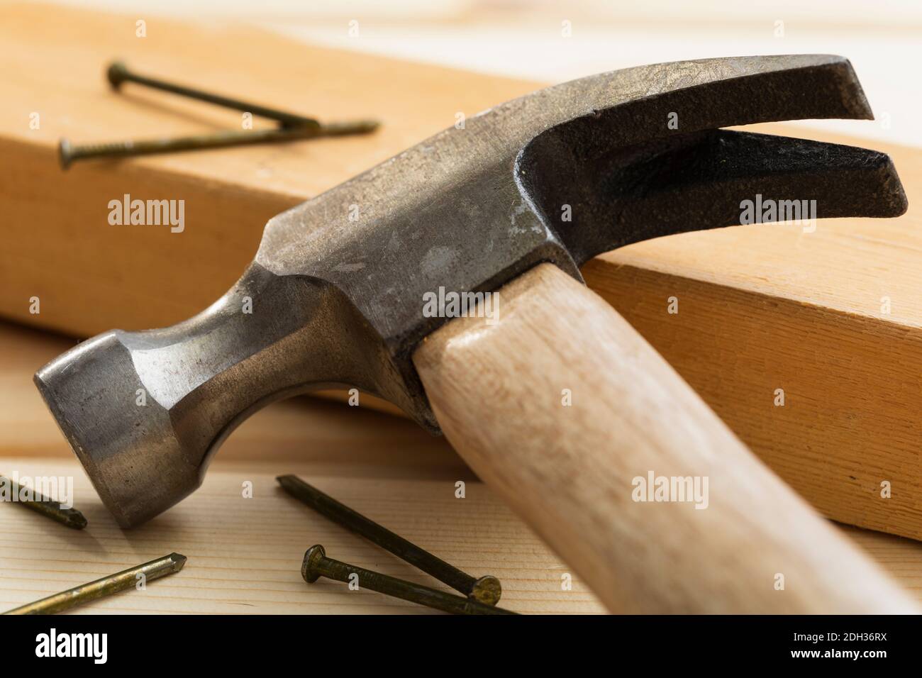 Nahaufnahme eines Hammers, der neben Nägeln auf einer Holzplanke an einem für den Bau vorbereiteten Arbeitsplatz liegt Stockfoto