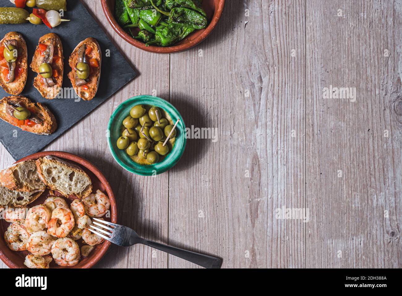 Obere horizontale Ansicht eines Holztisches mit Aufläufen mit Garnelen und grünen Paprika, ein Tablett mit kleinen Toasts mit rotem Pfeffer und Sardellen a vorbereitet Stockfoto