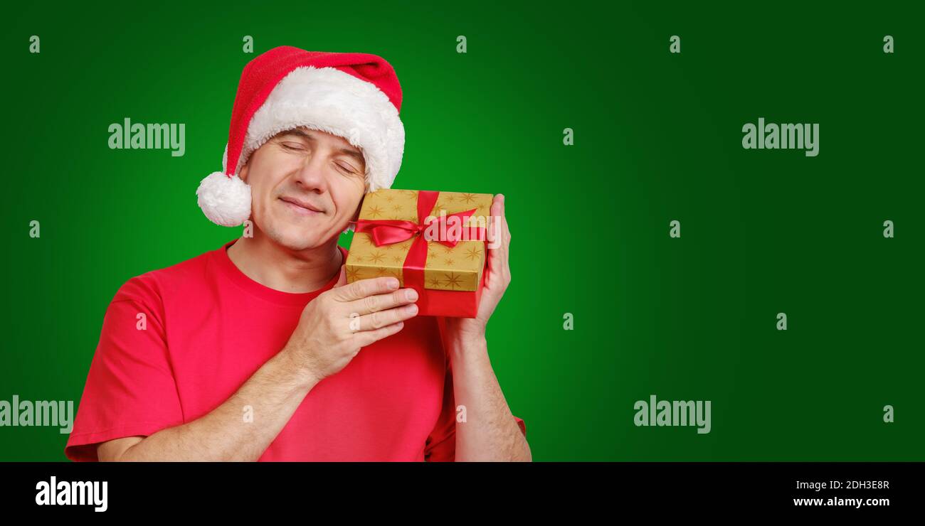 Mann in Santa Hut erhalten Weihnachtsgeschenk, hält in der Nähe seines Gesichts und lächelnd Stockfoto