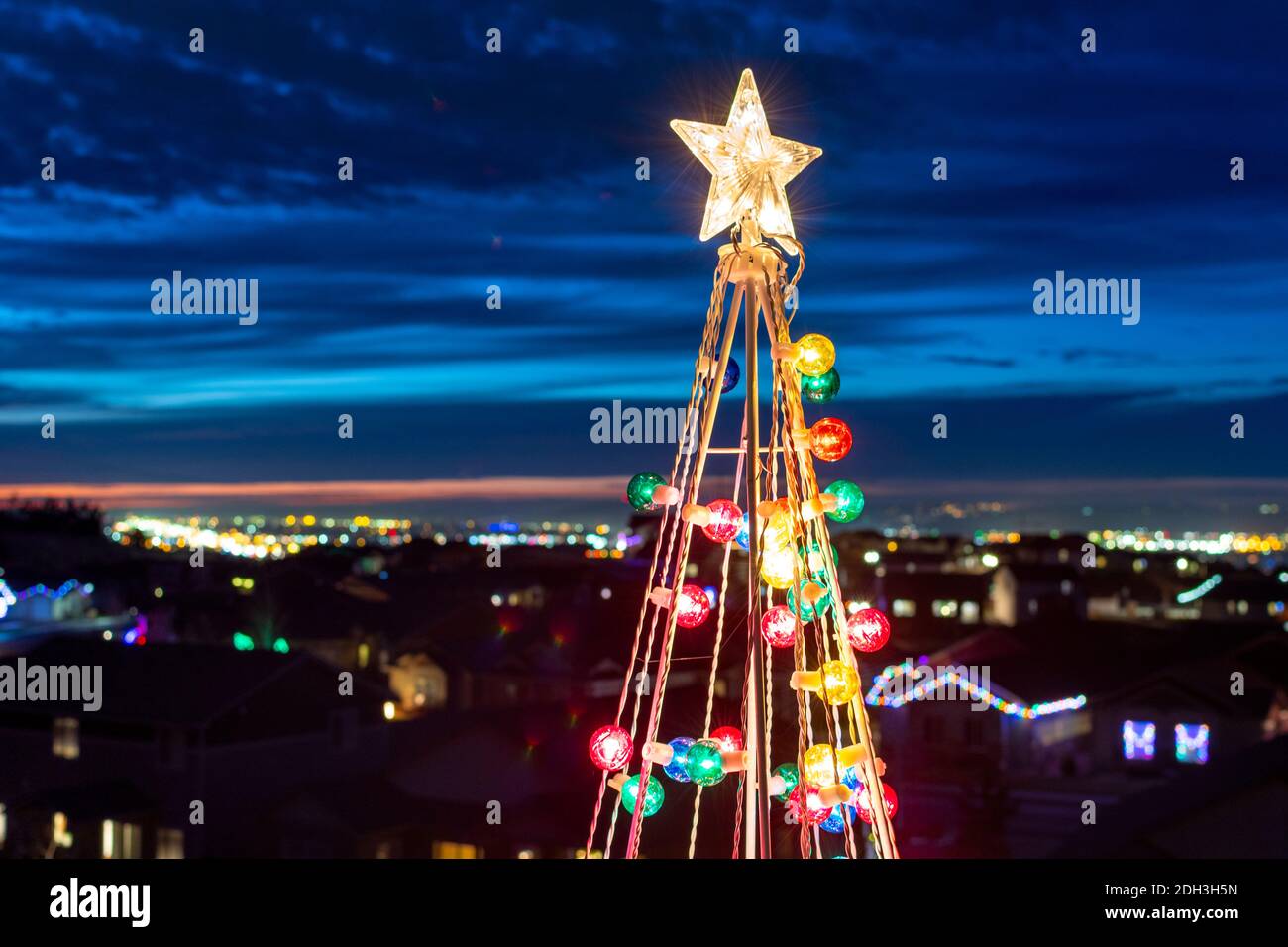 Nahaufnahme der Spitze einer beleuchteten Christbaumdekoration mit einem Stern und Ornamenten, mit einer Skyline von Spokane, Washington dahinter. Stockfoto