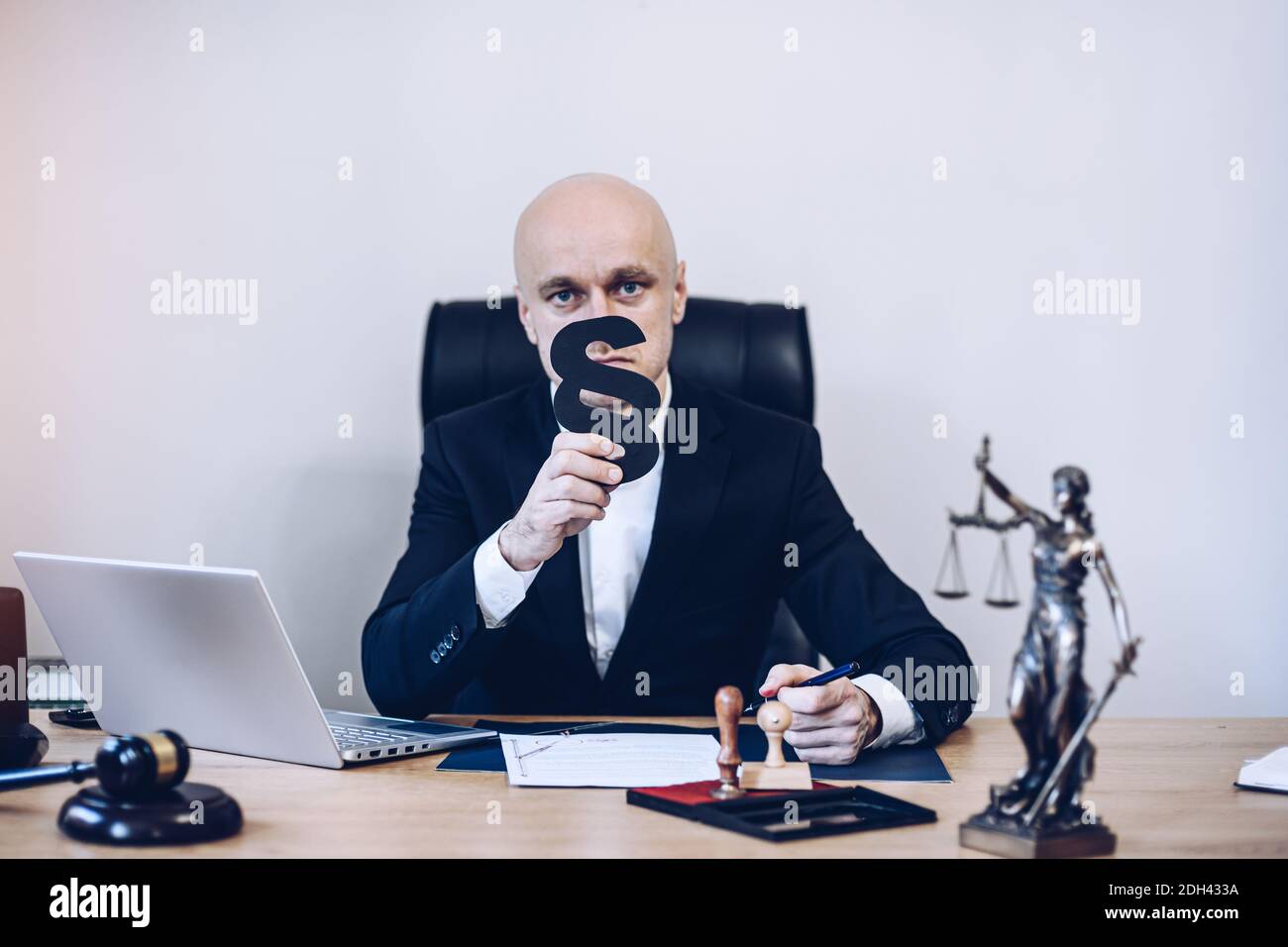 Ein hübscher Notar sitzt am Holztisch und hält als Zeichen von Recht und Ordnung einen Absatz in der Hand. Stockfoto