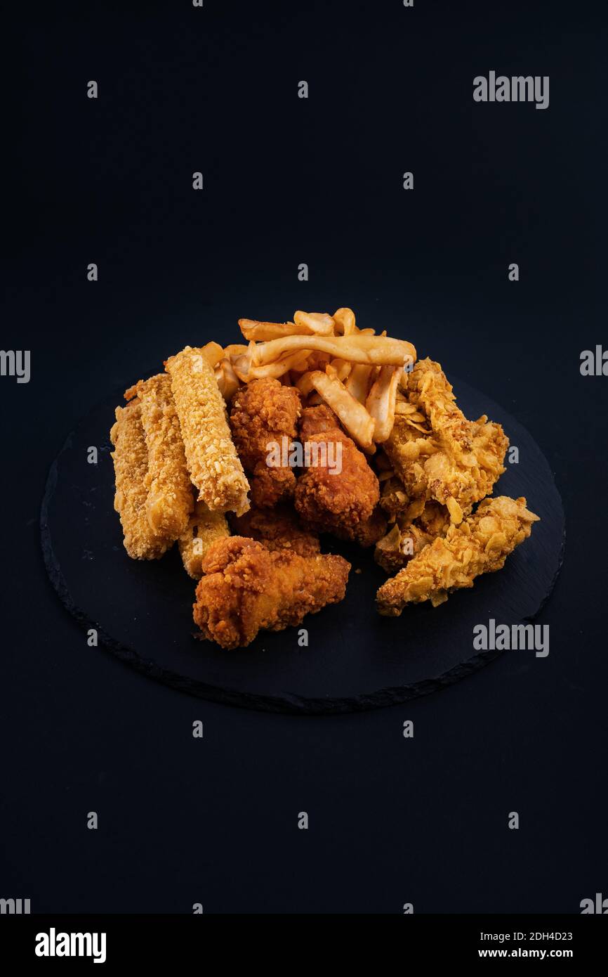 Eine Nahaufnahme eines schwarzen Serviertellers voller knuspriger Hähnchen, Tender, Nuggets und pommes Frites Stockfoto