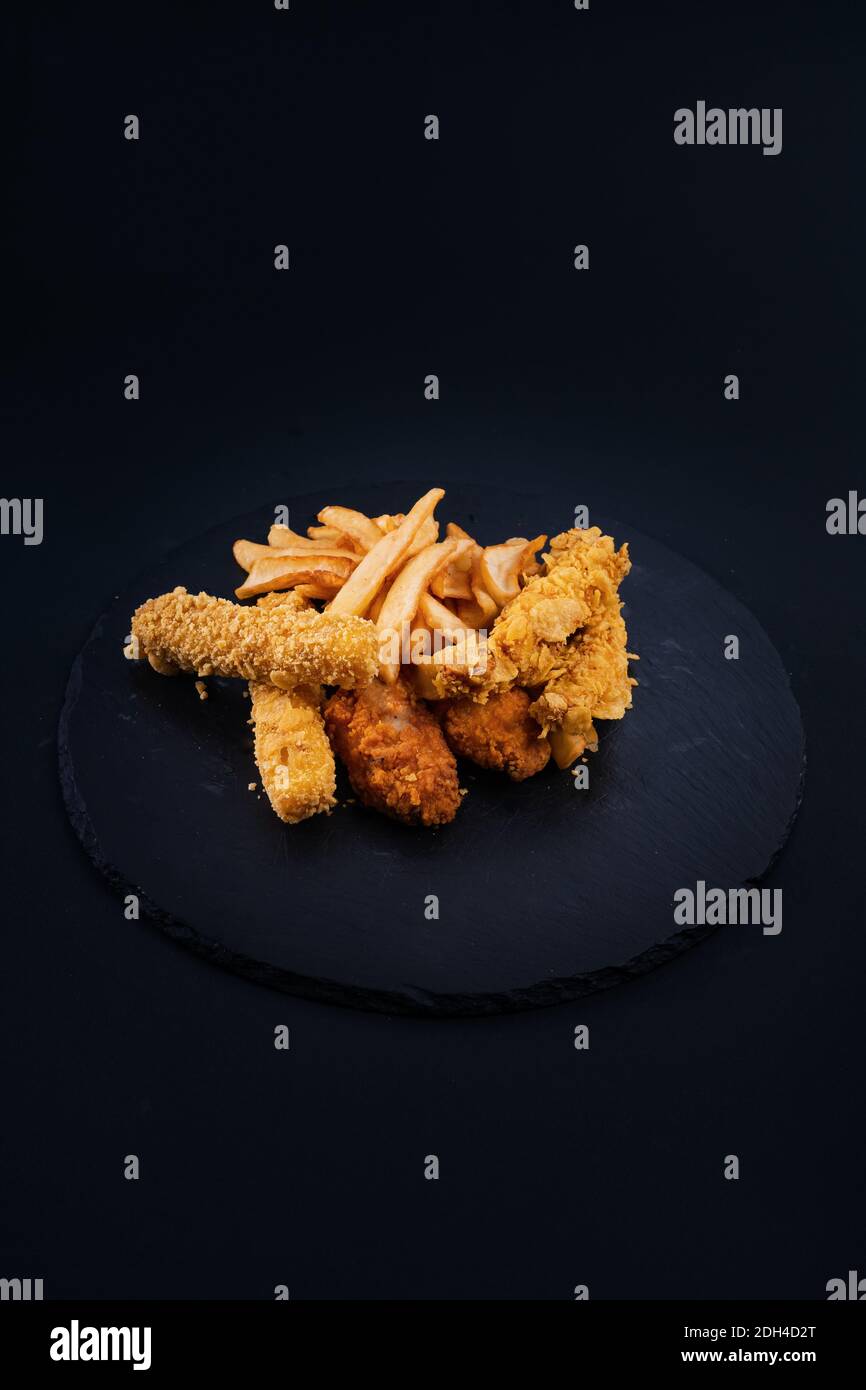 Eine Nahaufnahme eines schwarzen Serviertellers mit knusprigem Huhn, Tender, Nuggets und pommes frites Stockfoto