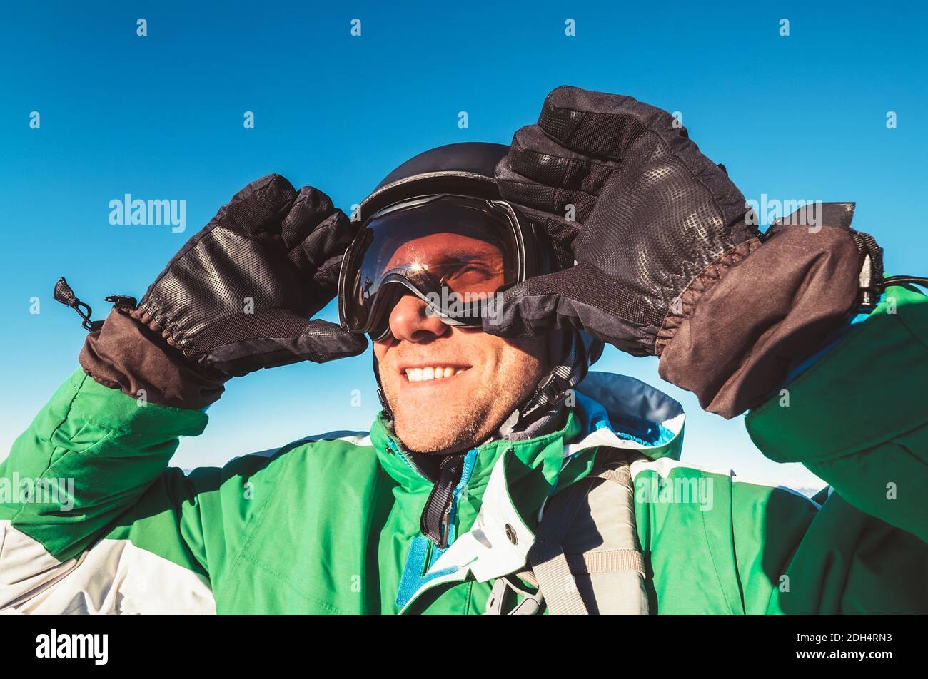 Lächelnder Skifahrer oder Snowboarder Mann Porträt in sicheren Skihelm und Brille mit blauem Himmel Hintergrund. Aktive Menschen oder aktive Ferien Konzeptbild. Stockfoto