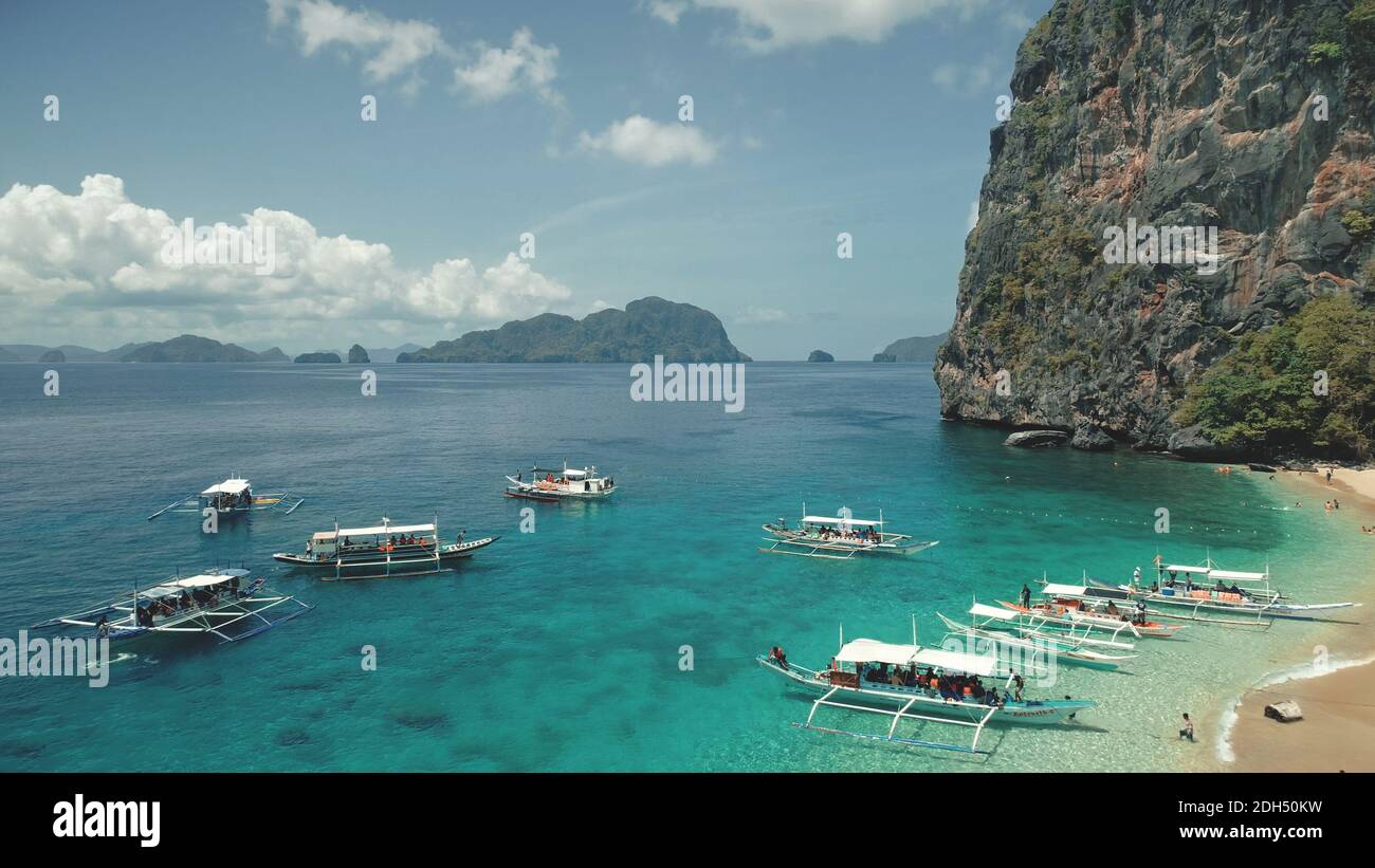 Tropische Meereslandschaft am Sandstrand mit ruhenden Touristen. Majestätische Hafenlandschaft auf der Insel El Nido, Philippinen, Asien. Nahaufnahme Passagierboot in Ocean Bay mit grünen Klippen Ufer in Luftaufnahme Stockfoto