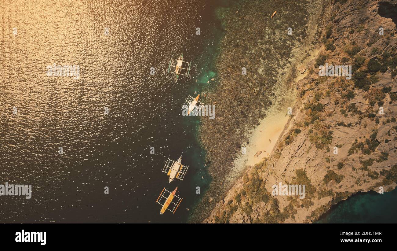 Top down der traditionellen philippinischen Passagierboote bei Sonnenuntergang Licht Luftaufnahme. Wassertransport an der Meeresbucht mit Sandstrand Küste der Berginsel Palawan. Dramatische dunkelblaue Meereslandschaft Stockfoto