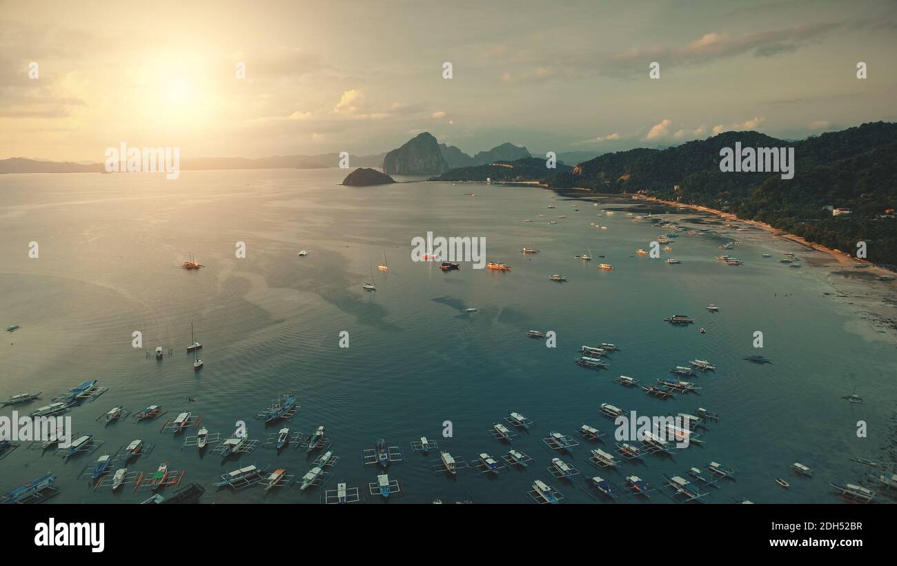 Sonnenuntergang an der Meeresbucht: Boote, Yachten am Wasser. Seascape an der Meeresküste mit Sandstrand, grüne Palmen auf Hügeln. Schiffstransport am Wasser am Sommerabend. Hügelige tropische Insellandschaft Stockfoto