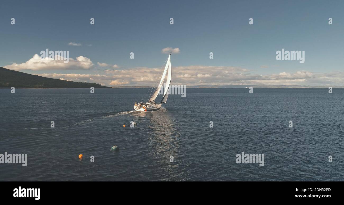 Erstaunliche Meereslandschaft der Meeresbucht mit Yacht-Antenne. Grüne Berginsel mit Wald am Nebelschwaden. Episches Segelboot am Seehafen von Brodick Pier, Arran Insel, Schottland, Europa. Sommerkreuzfahrt im Kino Stockfoto