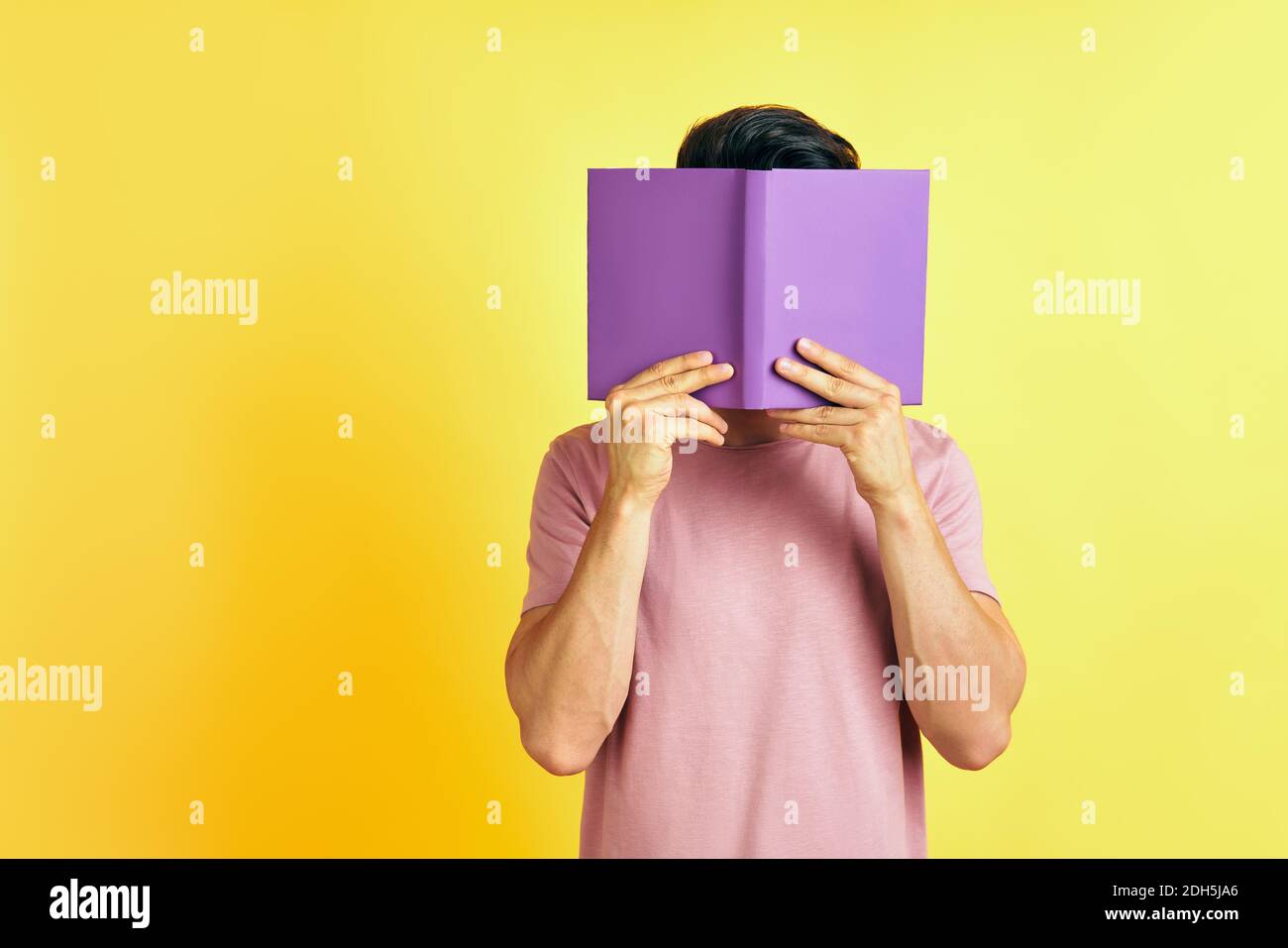 Der junge Mann versteckt sein Gesicht hinter einem Buch Stockfoto