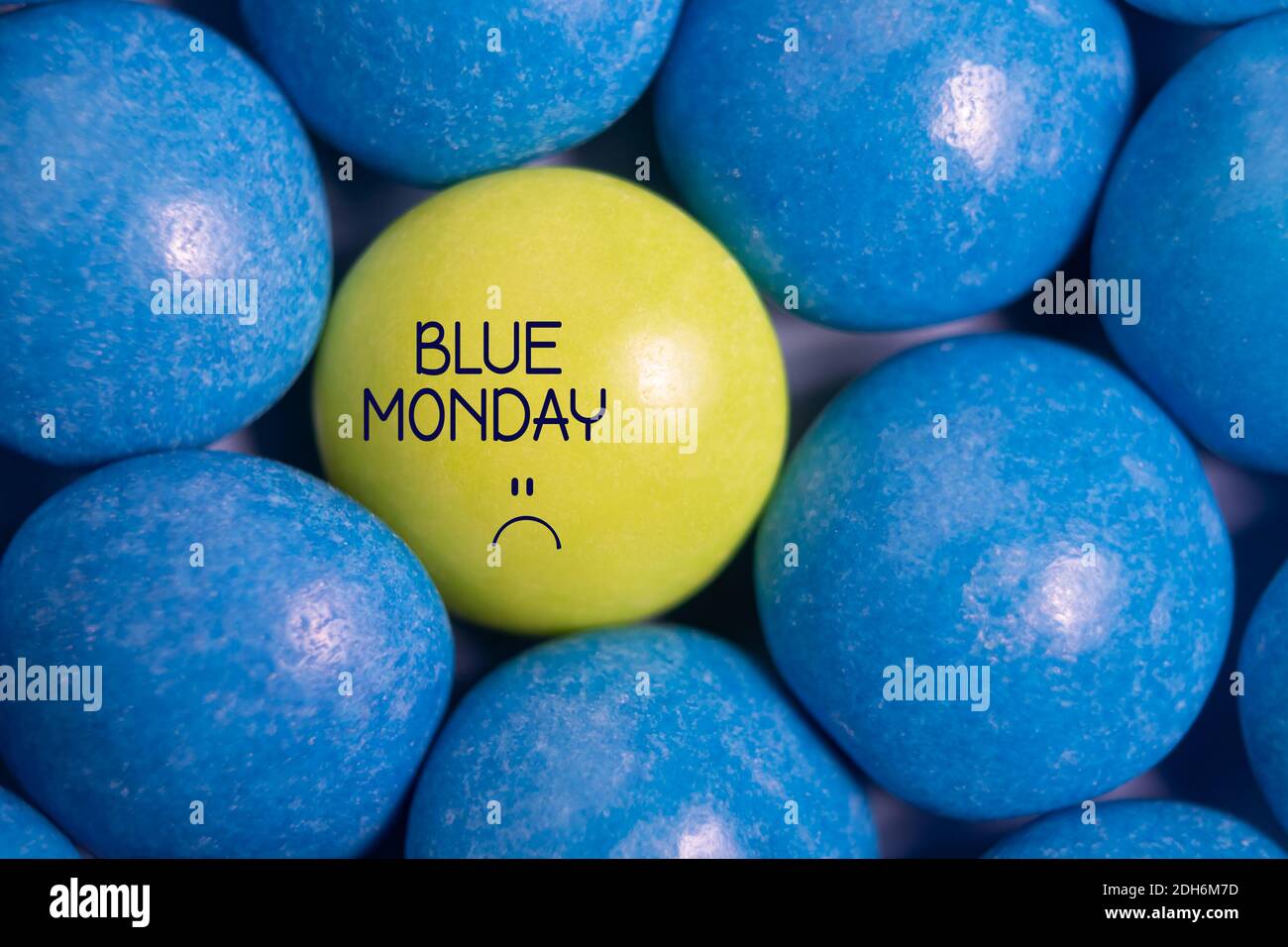 Blauer montagstext mit traurigem Smiley-Gesicht. Eine gelbe Süßigkeit in Blau. Der deprimierendste Tag des Jahres. Blue monday Konzept. Einfluss der Umwelt. Stockfoto
