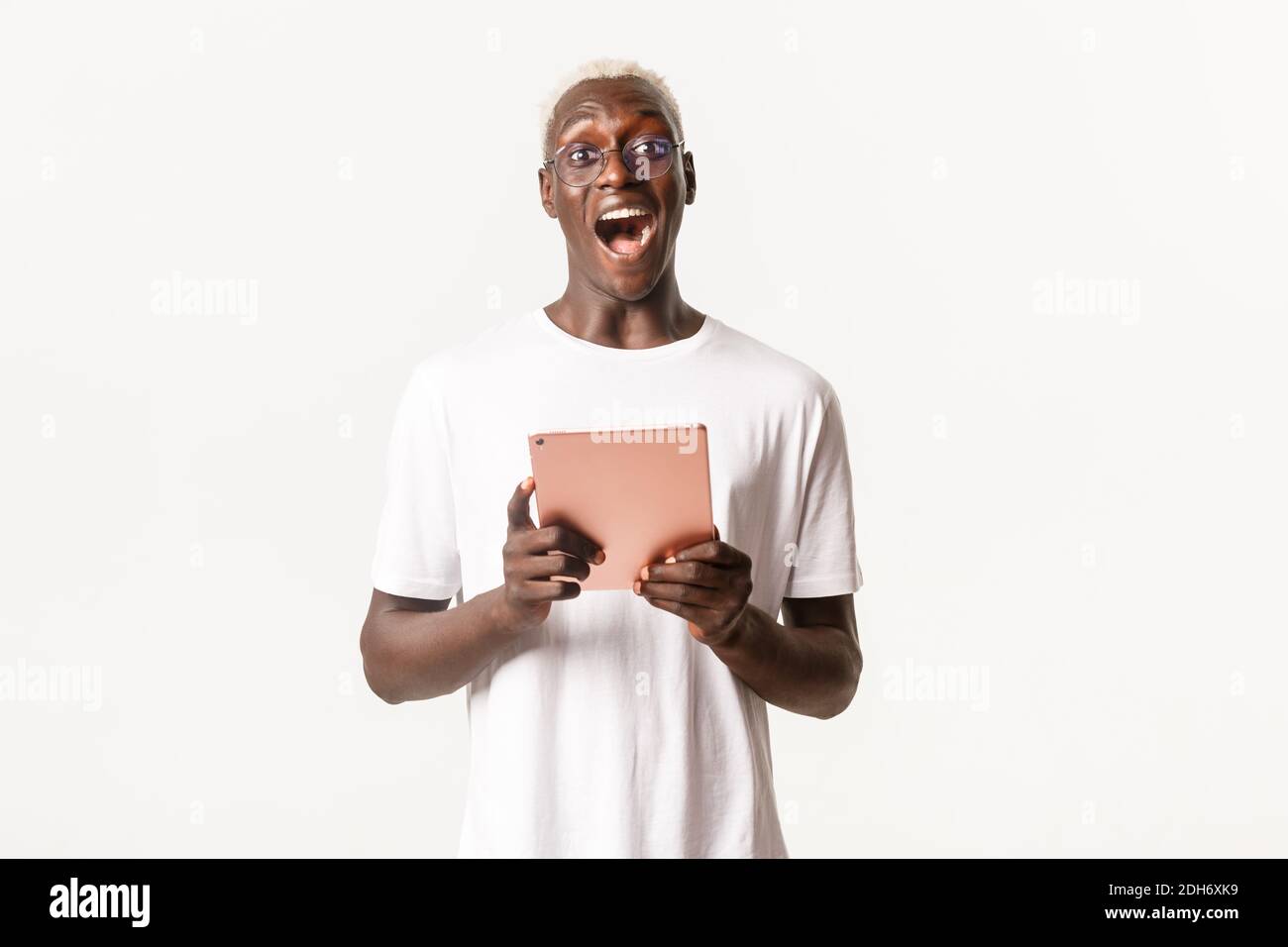 Portrait von aufgeregt gut aussehend afroamerikanischen männlichen Schüler in Brille, Blick erstaunt, halten digitale Tablette, stehend weiß BA Stockfoto