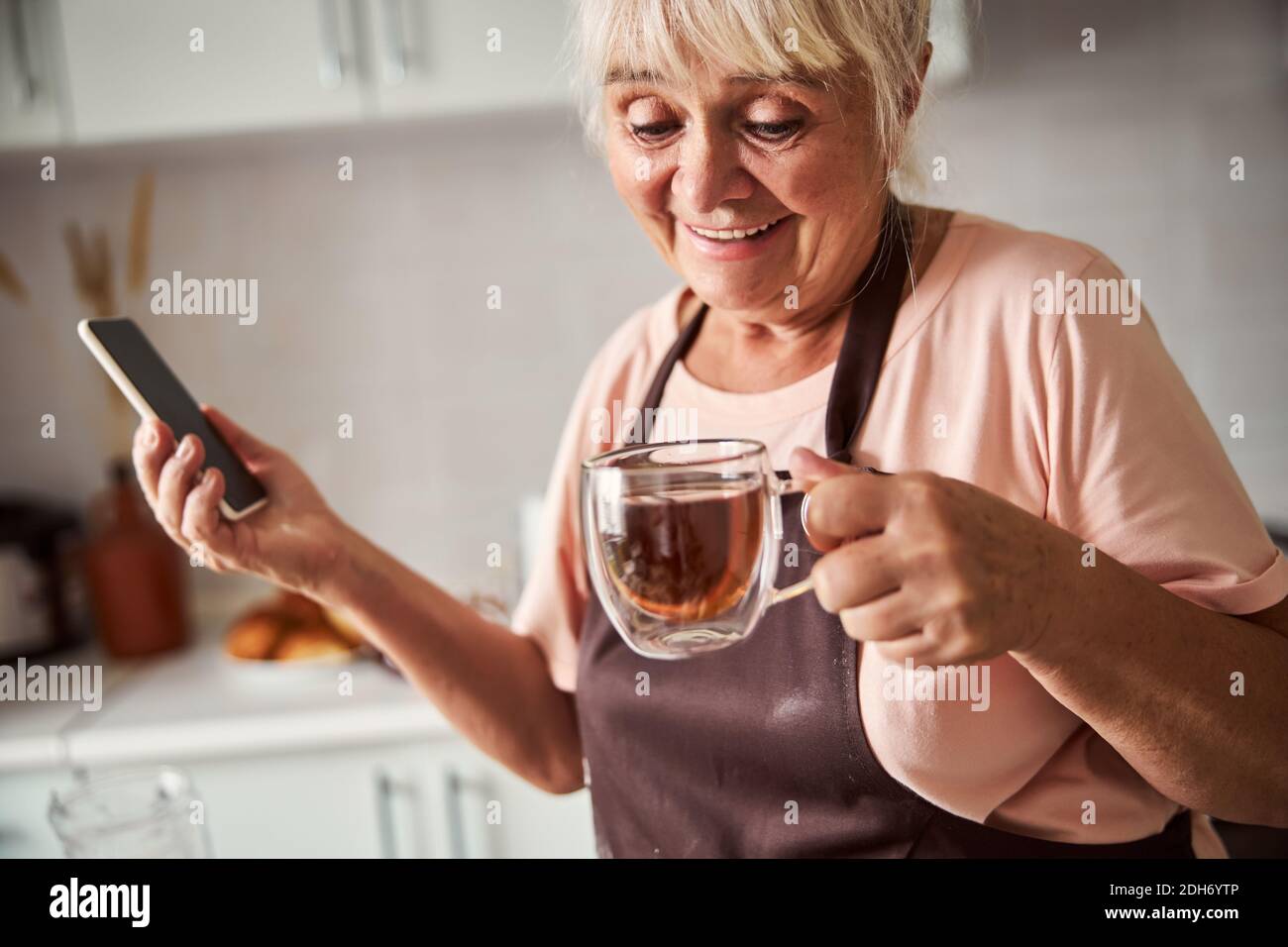 Aufgeregt ältere Frau mit heißen Tee in ihrer Küche Stockfoto