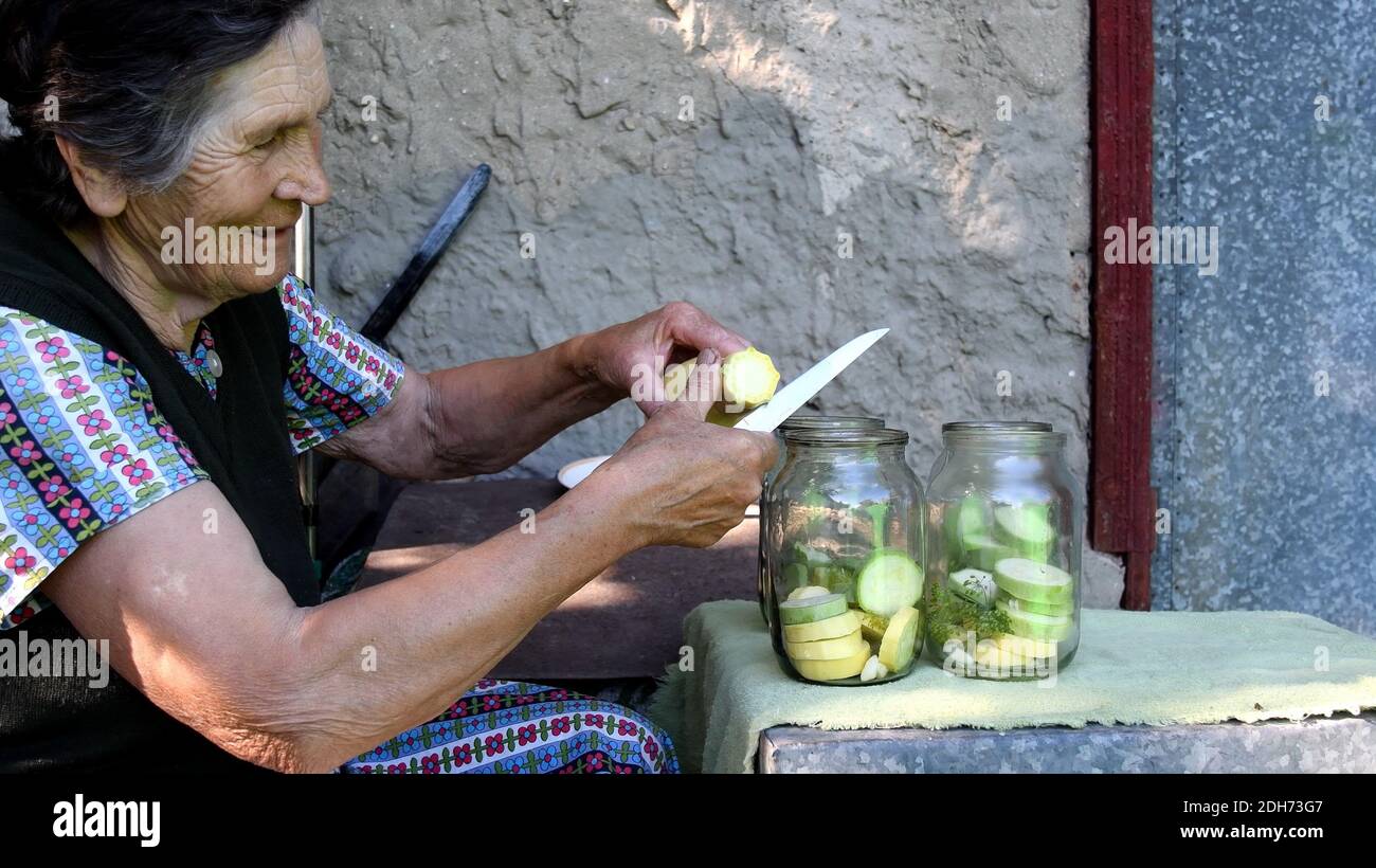 Faltige ältere Frau lächelt und schneidet rohen gelben Kürbis für hausgemachte Konserven mit Dillsamen und Knoblauch. Ländliche lokale Küche aus Bio-Gemüse Stockfoto
