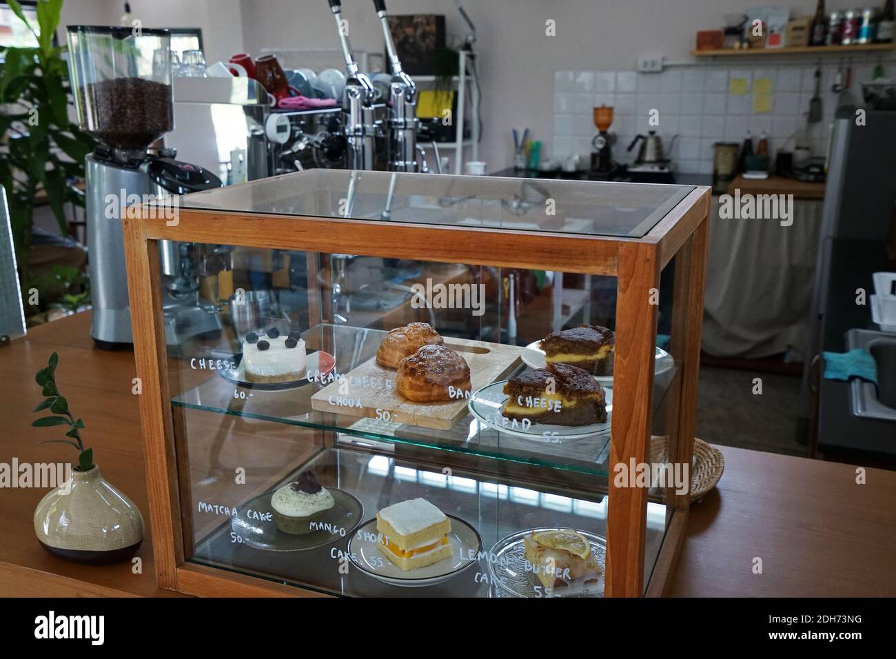 Eine hölzerne Vitrine mit Choux-Sahne, Zitronenbutterkuchen, Mango-Kurzkuchen, Matcha-Grüner Tee-Cupcake und Bananenkäse-Brot gefüllt Stockfoto
