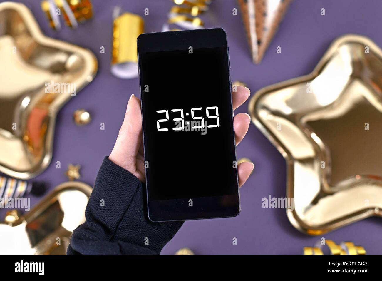 Konzept für Silvester Feier mit Hand halten smart Telefon mit Timer Countdown bis Mitternacht vor der Party Elemente im Hintergrund Stockfoto