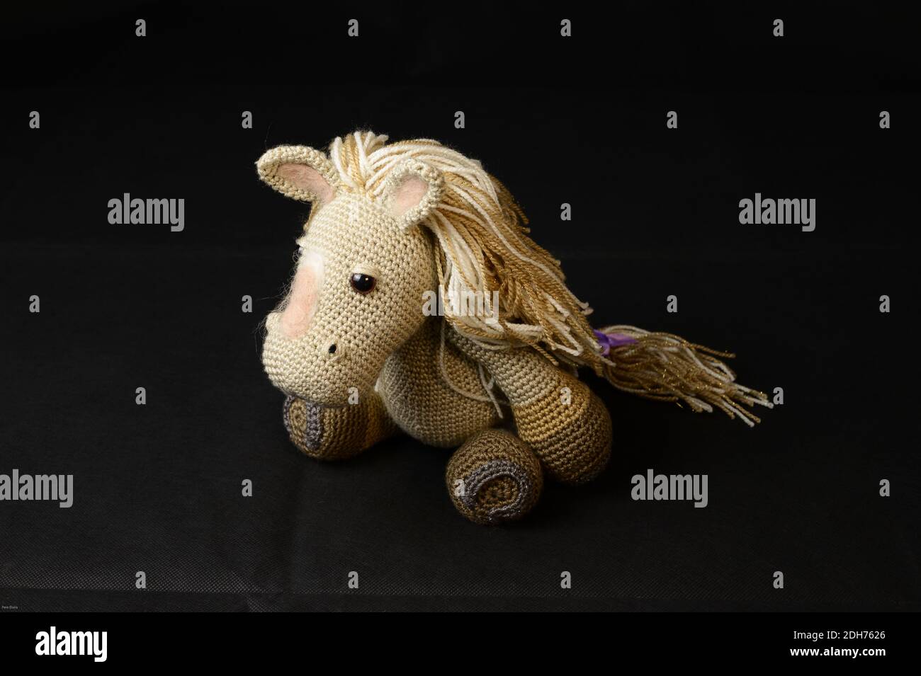 Ein gehäkeltes Amigurumi Pferd Spielzeug auf einem schwarzen Hintergrund Stockfoto