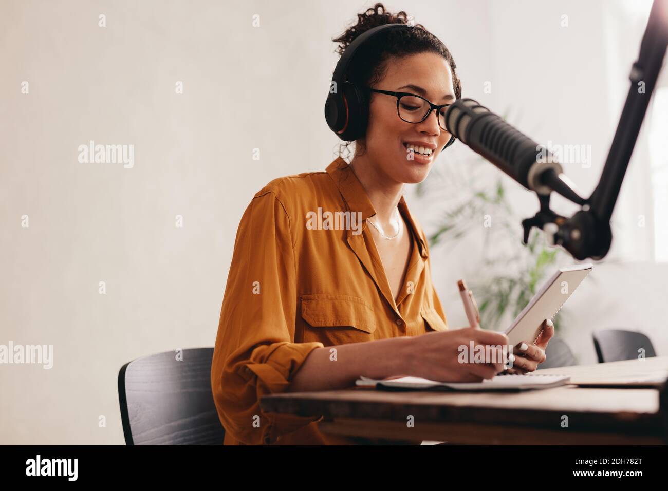 Junge Frau, die Podcast mit Mikrofon aufnimmt. Radio-Host, der von zu Hause aus arbeitet. Stockfoto