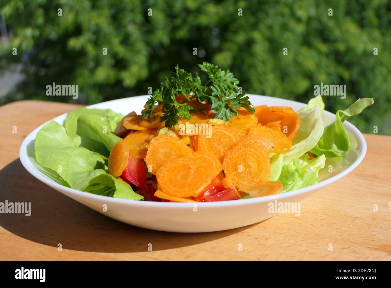 Köstlicher Salat mit frisch geschnittenen Karotten und Petersilie in einem Weiße Schale auf einem Holzteller Stockfoto