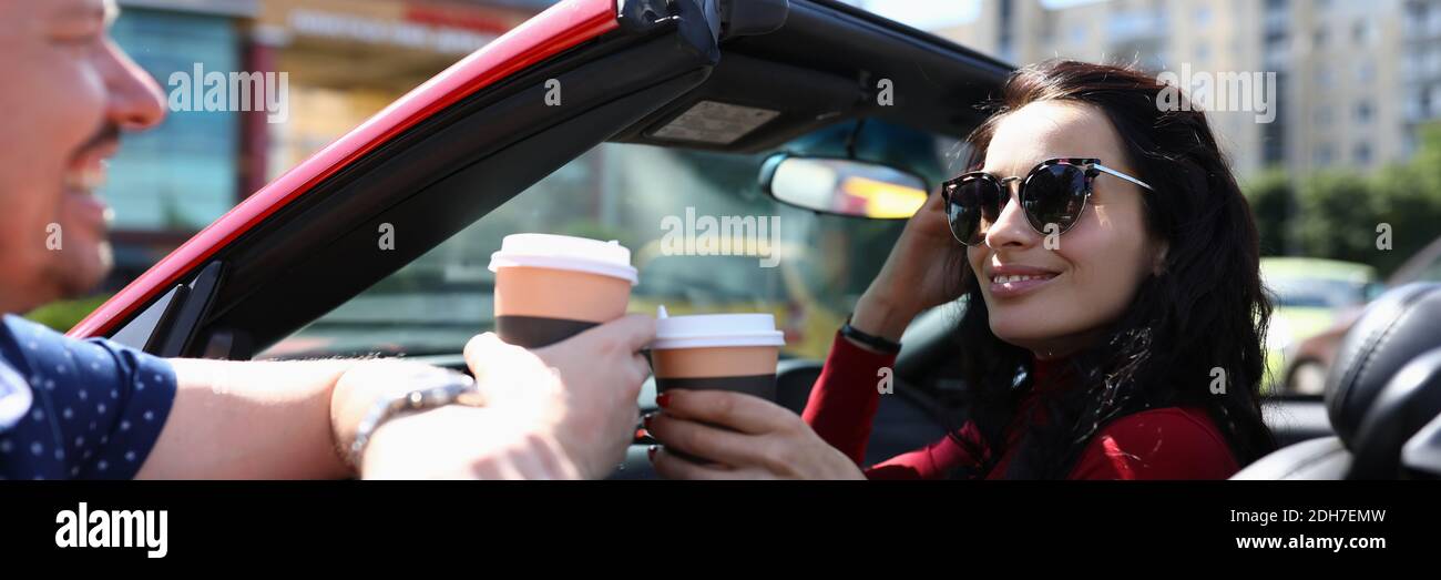 Frau in Sonnenbrille in rotem Cabrio trinkt Kaffee mit Mann Hochformat Stockfoto