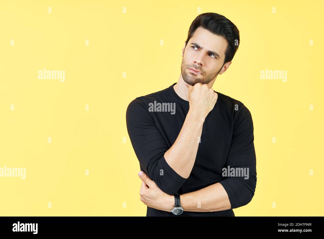 Junger nachdenklicher Mann denkt und schaut beiseite auf Kopierraum isoliert auf gelbem Hintergrund Stockfoto