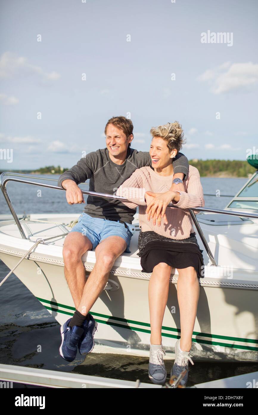 Glückliches Paar, das auf der Yacht gegen den Himmel sitzt Stockfoto