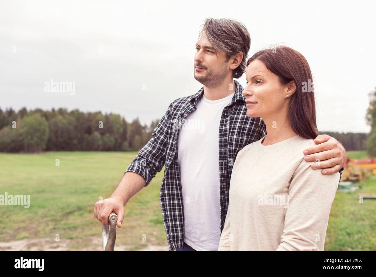 Nachdenkliches mittelerwachsenes Paar, das Arm herum auf organischem Bauernhof steht Stockfoto