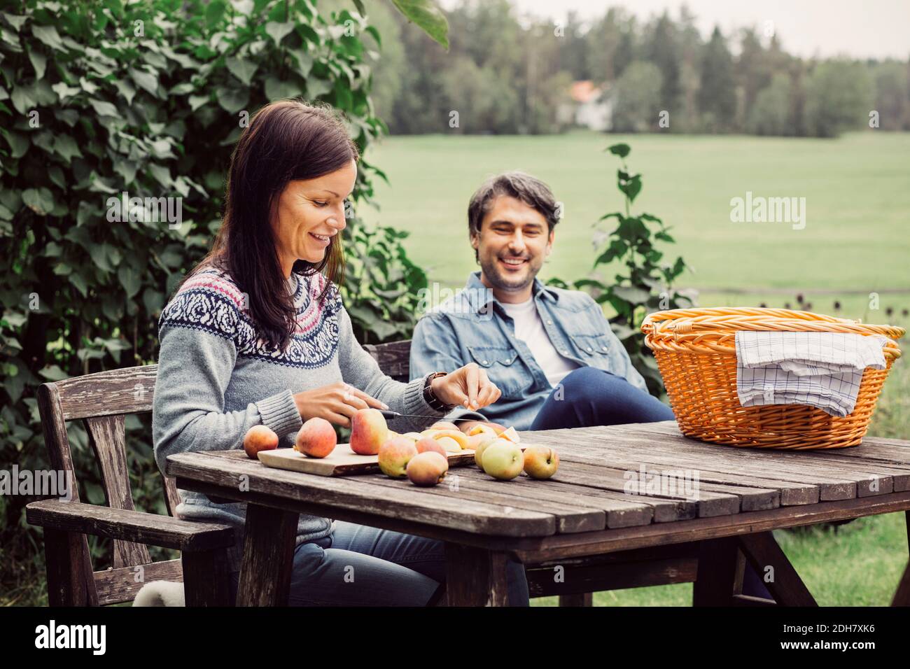 Glücklicher Mann, der die Frau beim Apfelschneiden am Tisch ansieht Bio-Bauernhof Stockfoto