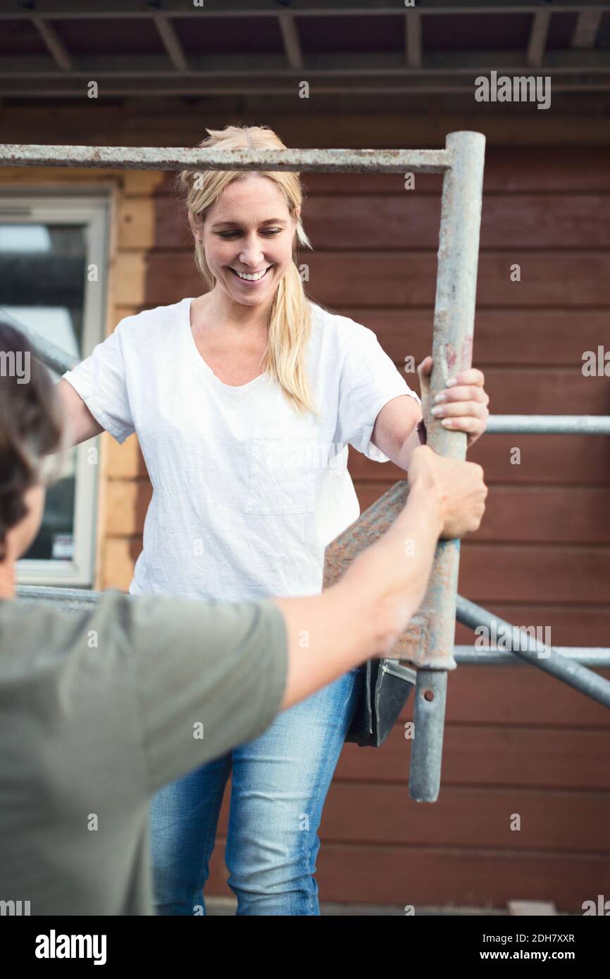 Lächelnde Frau mit Mann, der vor dem Haus am Gerüst arbeitet Renoviert Stockfoto