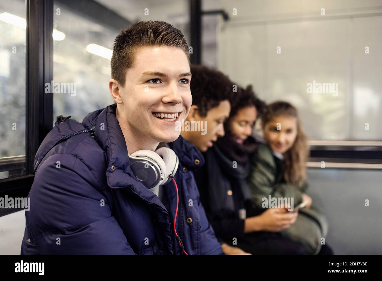 Glücklicher männlicher Universitätsstudent, der mit Freunden an der U-Bahn-Station sitzt Stockfoto