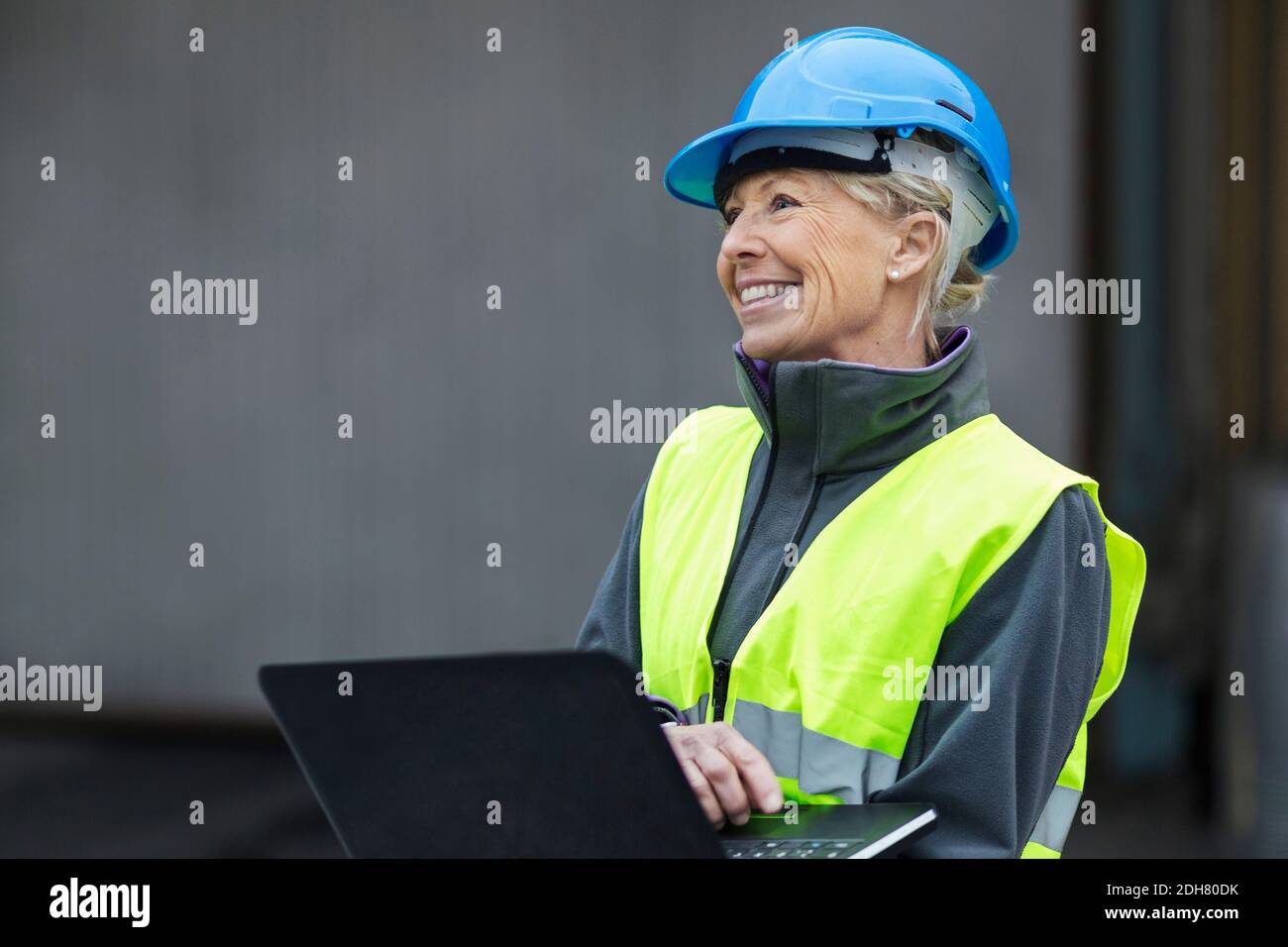 Glückliche reife weibliche Arbeiterin mit Laptop in der Fabrik Stockfoto