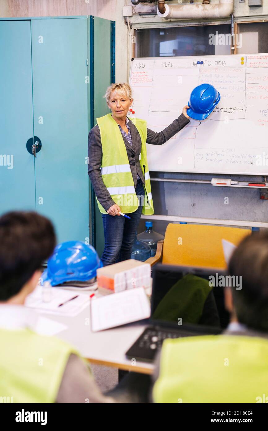 Reife weibliche Mitarbeiterin diskutiert Plan auf Whiteboard mit Kollegen in Werk Stockfoto