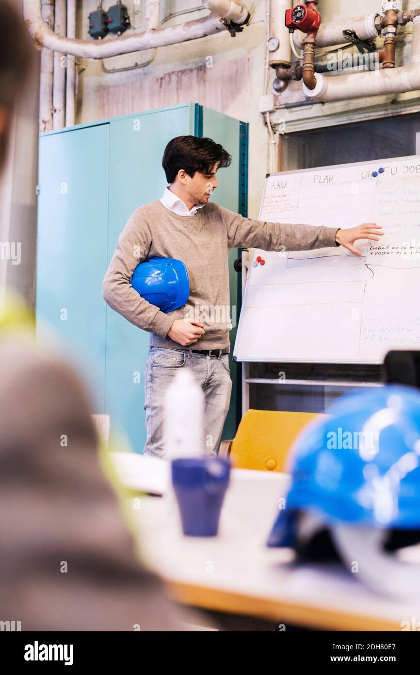 Junge männliche Arbeitnehmer diskutieren Plan auf Whiteboard zu Kollegen in Werk Stockfoto