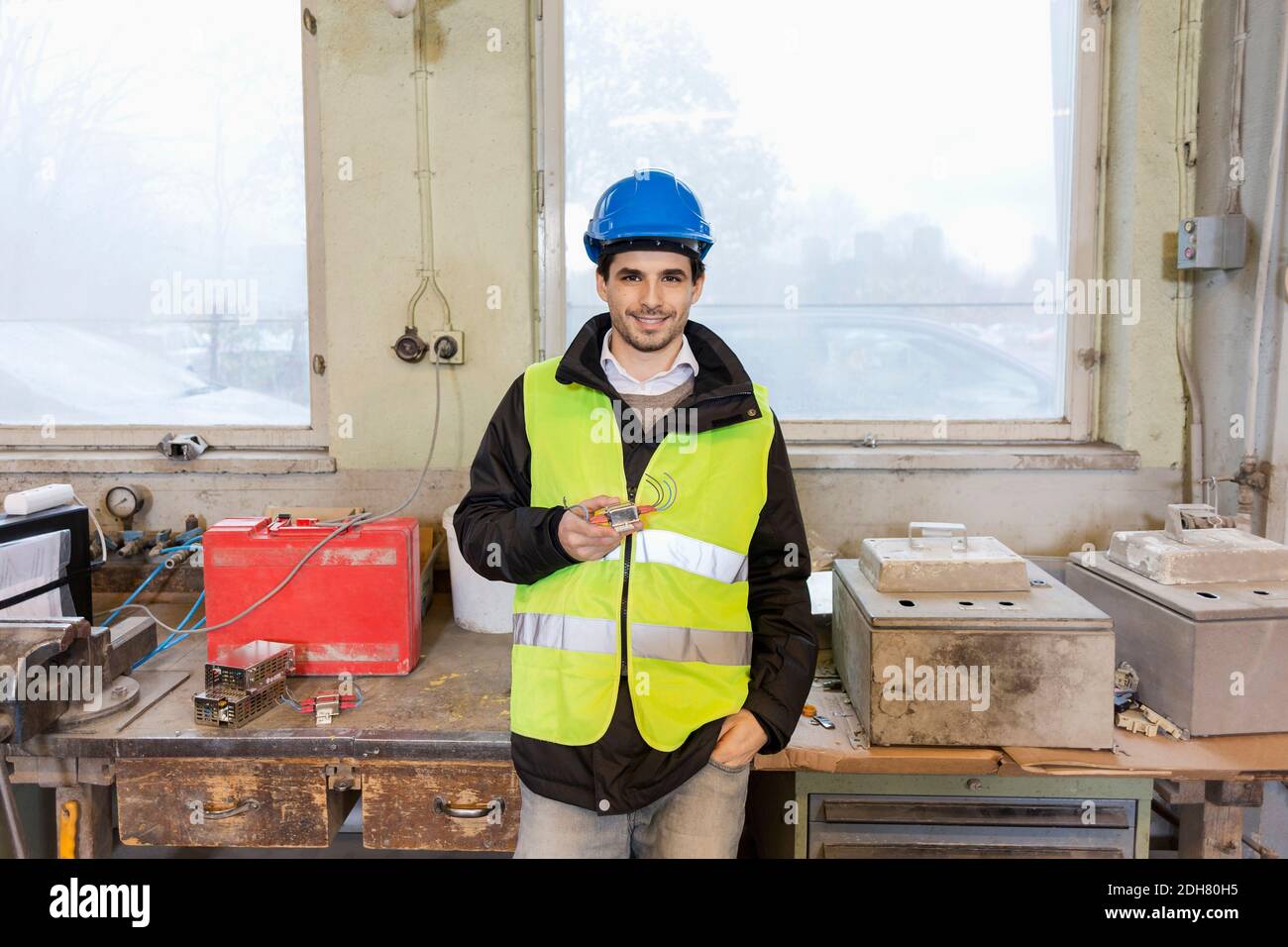 Portrait von selbstbewussten jungen manuellen Arbeiter halten Maschine Teil in Werk Stockfoto