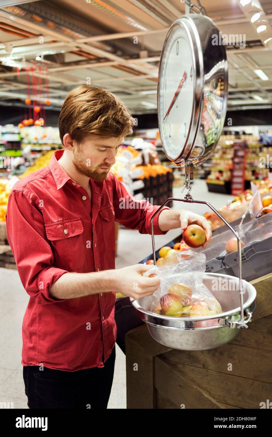 Junger Mann, der Äpfel im Supermarkt wiegt Stockfoto