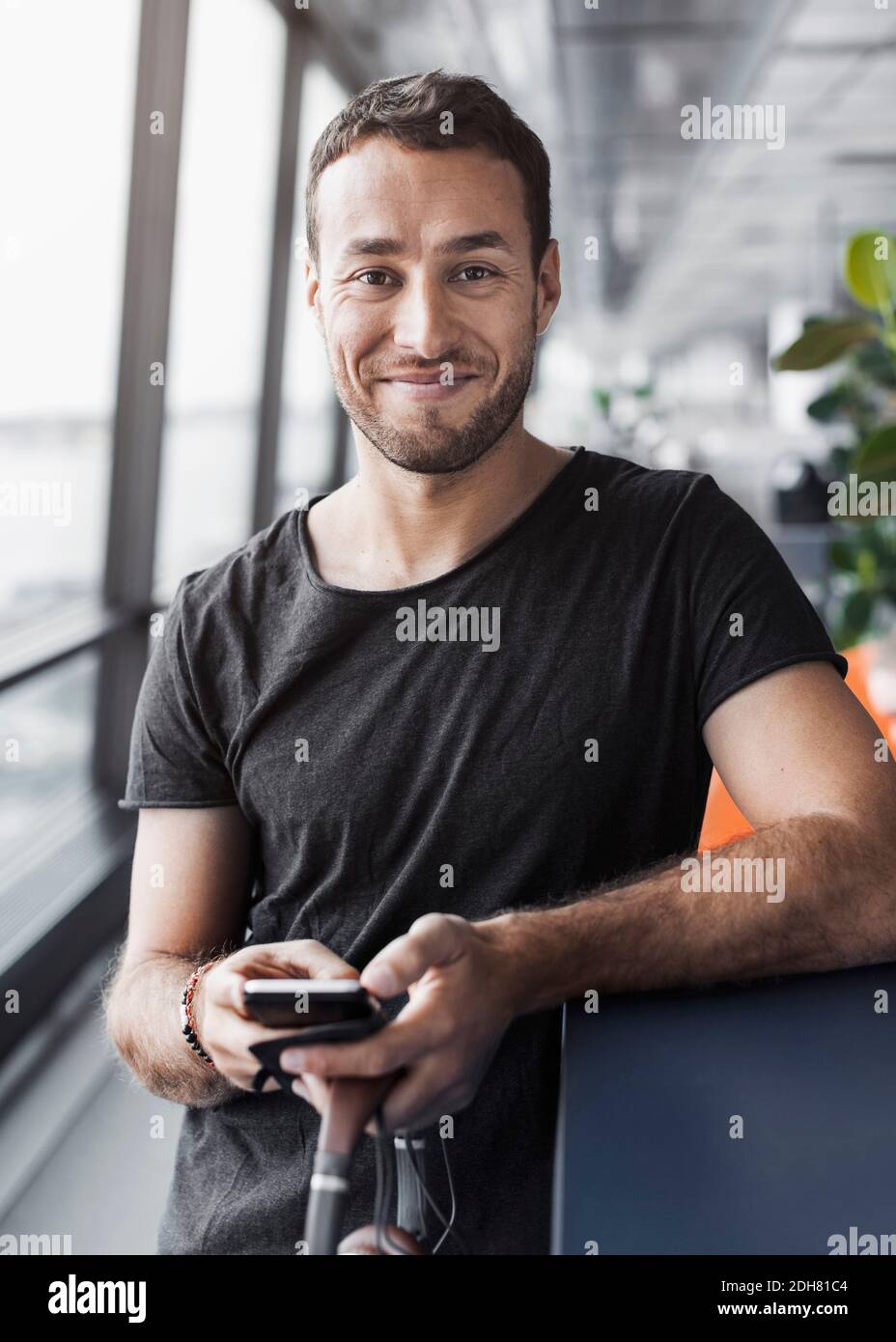 Porträt eines lächelnden Geschäftsmannes, der sein Mobiltelefon hält, während er sich darauf stützt Arbeitsplatz im Büro Stockfoto