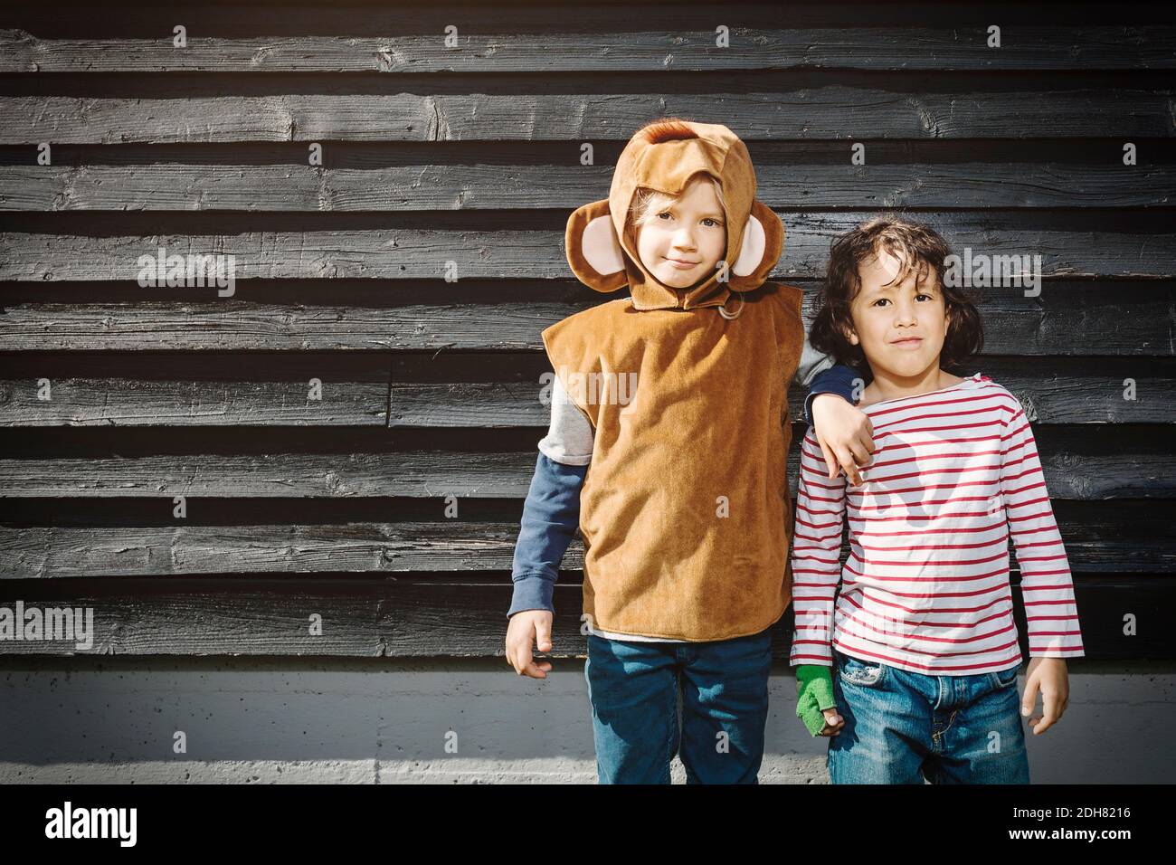 Mädchen im Affenanzug stehen mit Freund gegen schwarze Holz Wand Stockfoto